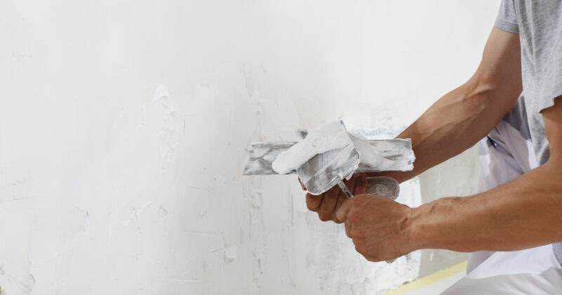 Hands man plasterer construction worker at work with trowel, plastering a wall, closeup